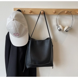 Close-up of black lychee grain leather bucket bag hanging on a wooden wall hook