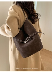 Détail d'un grand sac seau en daim marron foncé avec sangle en cuir sur l'épaule d'un mannequin
