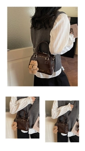 Detail of dark brown glossy Boston bag with embossed letters and plush bear charm