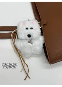 Close-up of a white fluffy puppy charm with silver bone tag on a brown leather tote bag