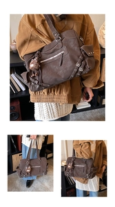 Detail of dark brown retro tote bag with utility buckles and plush doll pendant