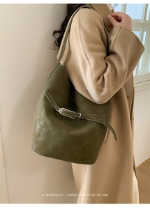 Gros plan sur un sac seau en cuir vert foncé porté avec un manteau en laine camel