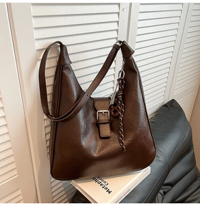 Detail of dark brown leather tote bag with metallic buckle and woven rope pendant