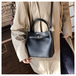 Close-up of black lychee grain bucket bag with metal lock detail and handle on a model
