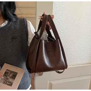 Detail der dunkelbraunen Leder-Eimertasche mit geprägtem Logo und schützenden Metallfüßen
