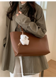 Brown faux leather tote bag with plush bear charm worn on shoulder for commute