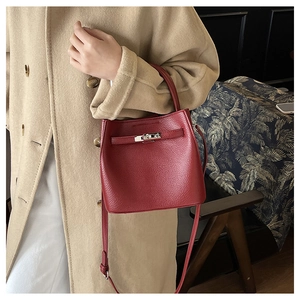 Detail of burgundy pebbled leather bucket bag with silver twist lock on beige coat