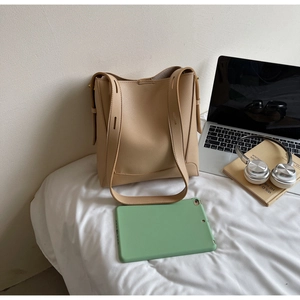 Detail of minimalist cream-colored leather bucket bag with pebble texture and wide strap