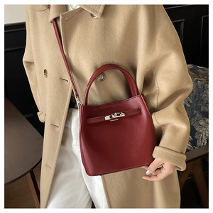 Close-up of red lychee leather bucket bag with silver metal turn-lock on wool coat
