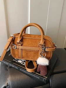 Sac Boston en daim marron avec garniture en cuir et breloque gant sur un livre