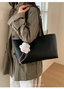 Minimalist black leather tote bag with white floral charm worn on khaki trench coat