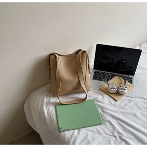 Close-up of beige tote bag made of lychee grain leather with books and gadgets