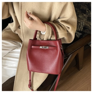 Close-up of burgundy litchi grain leather bag with metallic twist-lock on camel wool coat