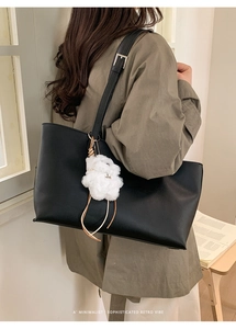 Detail of black pebbled faux leather tote bag featuring a cute white plush puppy charm