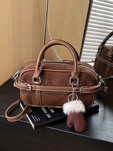 Sac Boston vintage en daim marron avec breloque gant sur un livre noir et ombre