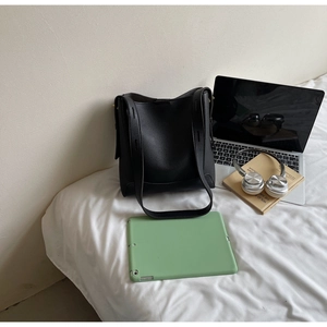 Close-up of black lychee grain leather tote bag with wide strap on a cozy bed setup