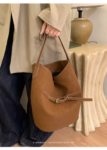 Détail d'un sac seau en cuir marron avec sangle à boucle rétro et design épuré
