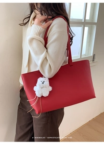 Detail of red leather tote bag with a white plush bear charm on a minimalist background