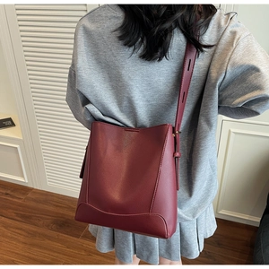 Minimalist burgundy bucket bag in litchi grain leather shown on model's shoulder