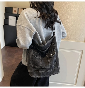 Dettaglio di una grande borsa a tracolla in denim nero lavato con cuciture e tasche utility
