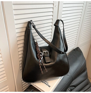 Macro view of black hobo bag with smooth texture and metallic buckle on white books
