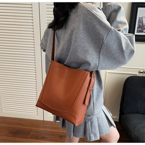 Detailed side view of brown leather bucket bag with adjustable strap and metallic hardware