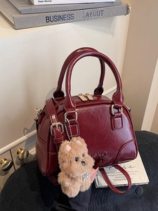 Retro burgundy Boston handbag with shiny finish and cute puppy charm on a sofa