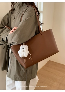 Detail of a large brown leather tote bag with a white plush dog charm on a model