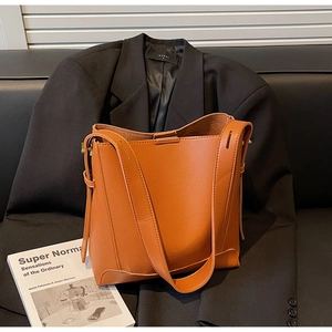 Close-up of orange-brown lychee grain leather bucket bag on a black sofa setting