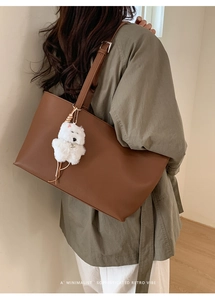Detail of dark brown leather tote bag texture with a cute white plush puppy charm