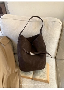 Détail du sac seau en daim marron foncé avec surpiqûres blanches contrastées sur canapé