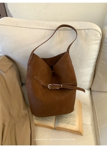 Détail d'un sac seau rétro marron avec texture cuir et boucle sur un livre vintage