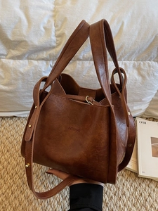 Braune Vintage Eimertasche mit Henkeln und Nietenschultergurt auf dem Bett