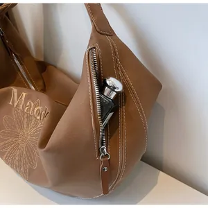 Dettaglio borsa a spalla marrone in pelle con tasca zip laterale e ricamo a margherita