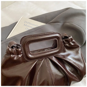 Detail of dark brown glossy bag with pleated texture and unique rectangular handle