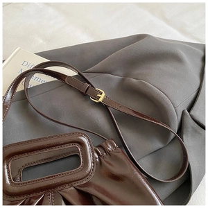 Close-up of deep brown glossy pleated cloud bag with rectangular handle and golden buckle