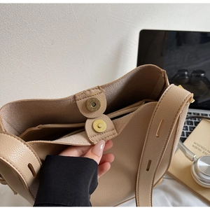 Detail of adjustable strap and magnetic closure on beige pebbled leather bucket bag