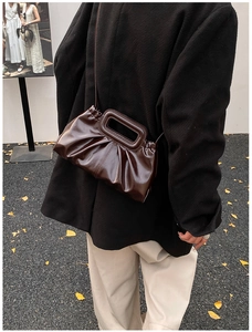 Dark brown pleated tote bag with unique rectangular handle shown on shoulder with black coat