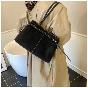 Detail of a black suede tote bag with white contrast stitching and a buckle strap