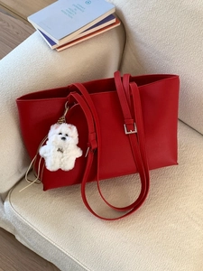 Large red leather tote bag with lychee texture and cute white puppy charm on a soft sofa