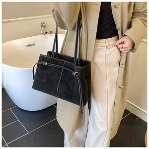 Close-up of black suede tote bag featuring white contrast stitching and silver metal buckle