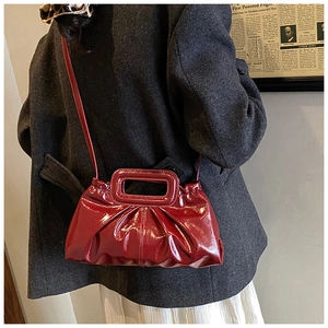 Detail of red pleated patent leather tote bag with unique cutout handle and long strap