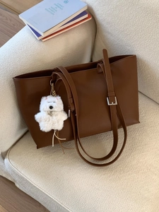 Minimalist caramel brown large tote bag with bear charm on a beige textured sofa