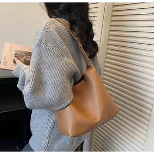 Brown leather bucket bag with pebble texture and adjustable wide strap shown on shoulder