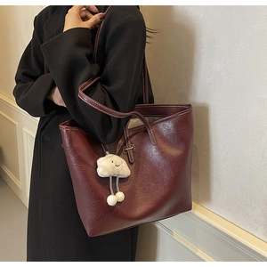 Detail view of large burgundy faux leather tote bag with white contrast stitching and charm