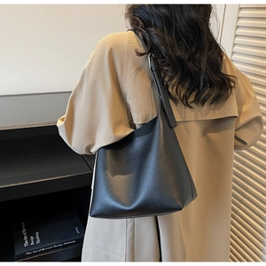Detail of black litchi grain leather shoulder bag with adjustable strap on a model