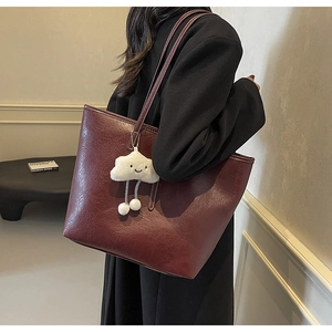 Detail of burgundy leather tote bag with white cloud plush charm in minimalist setting