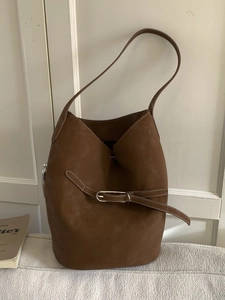 Sac seau vintage en daim marron avec fine bandoulière et boucle argentée sur un canapé
