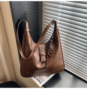 Detail of a brown Hobo bag with textured faux leather, buckle and decorative pendants