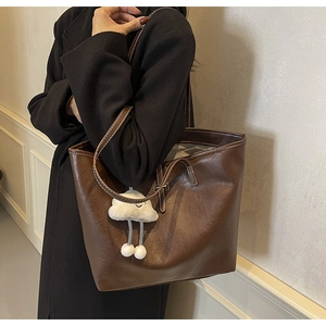 Detail view of brown faux leather tote bag with white stitching and plush cloud charm